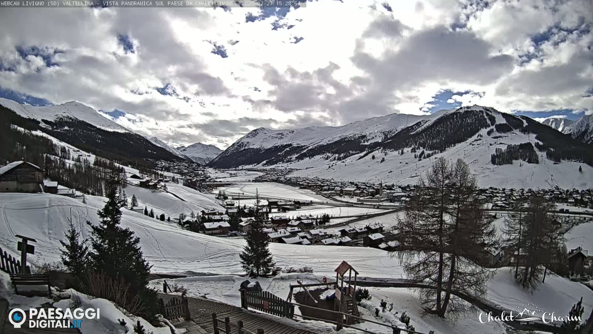 A snow-covered mountain village is viewed from a hillside on a partly cloudy day.