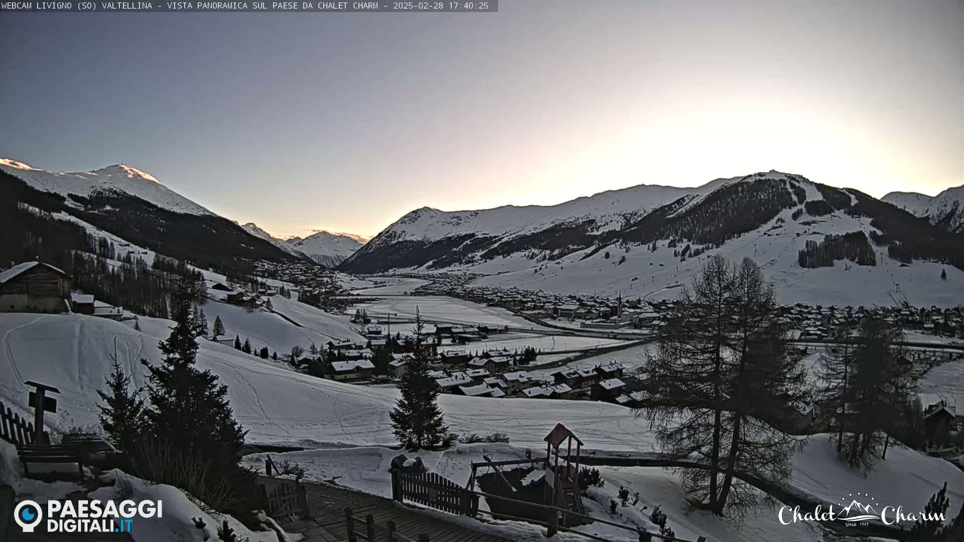 A snow-covered valley town nestled among snow-capped mountains under a twilight sky.