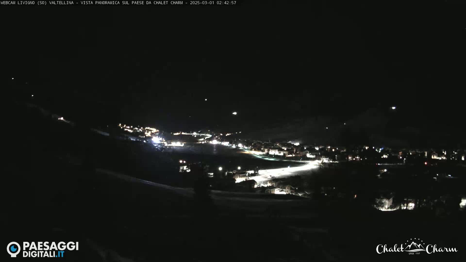 A nighttime panoramic view of a town illuminated by streetlights under a clear, dark sky.