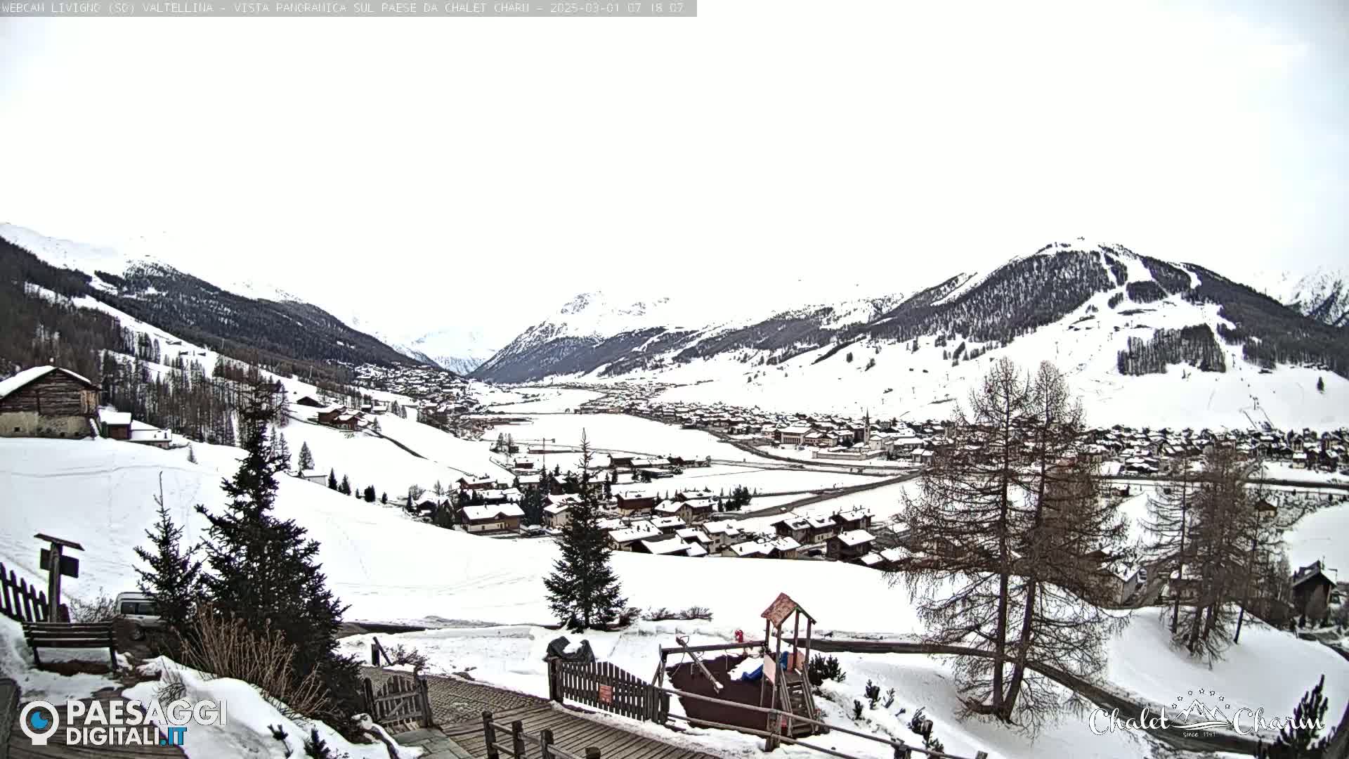 A snow-covered village nestled in a valley between snow-capped mountains on an overcast day.