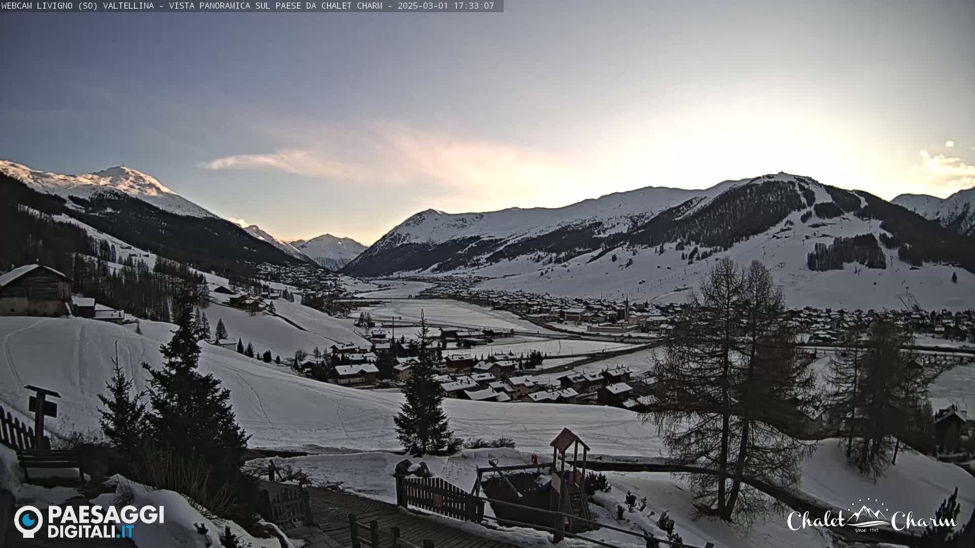A snow-covered mountain village is seen at sunset, with a mostly clear sky and some faint clouds.