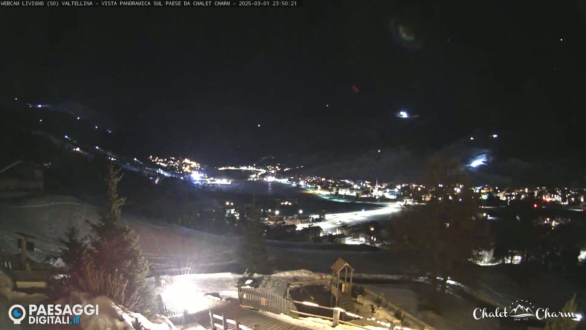 A nighttime, panoramic view of a snow-covered town illuminated by lights, with a clear sky speckled with stars.