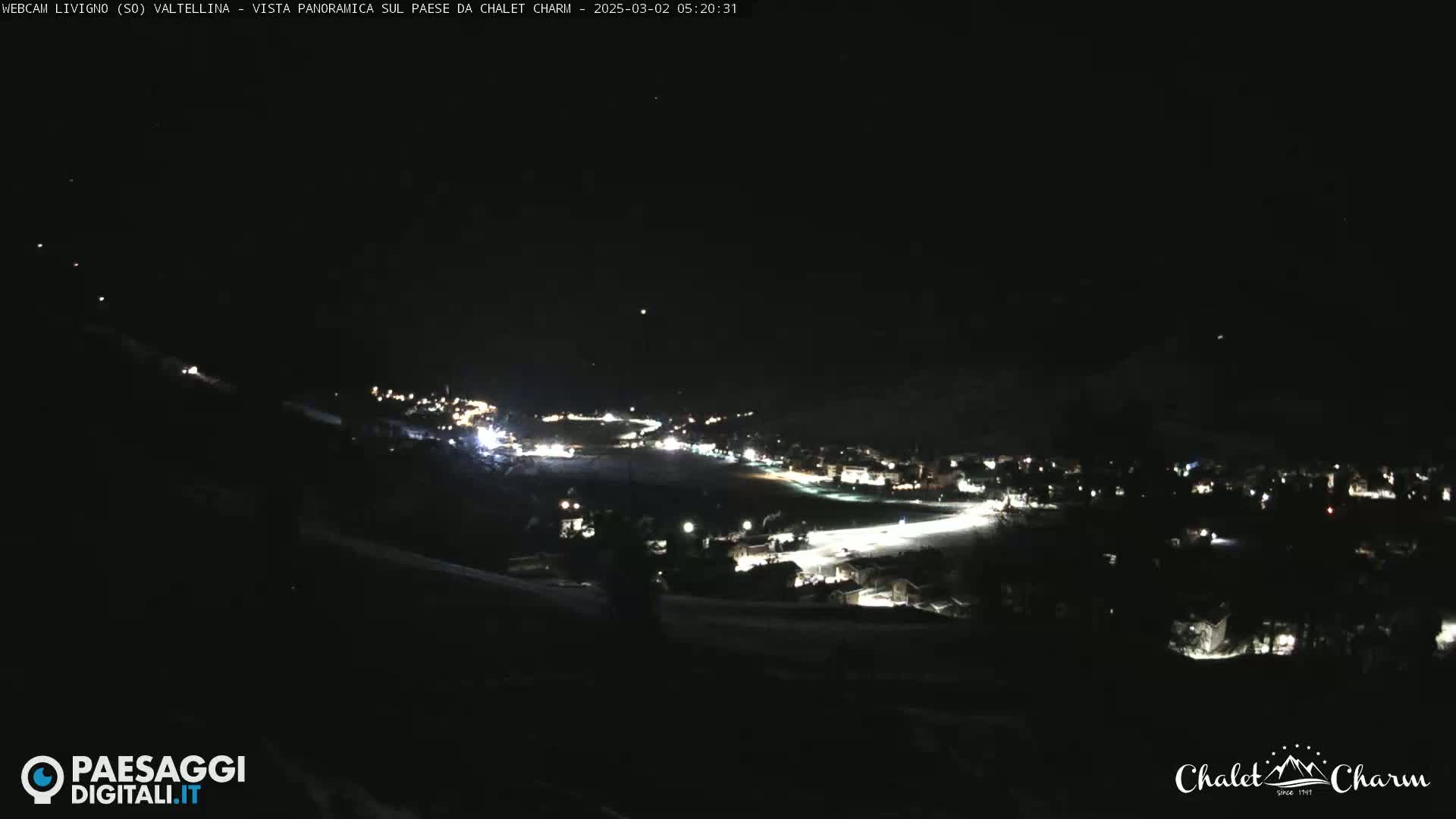 A nighttime, panoramic view of a snow-covered village illuminated by scattered lights under a clear, dark sky.
