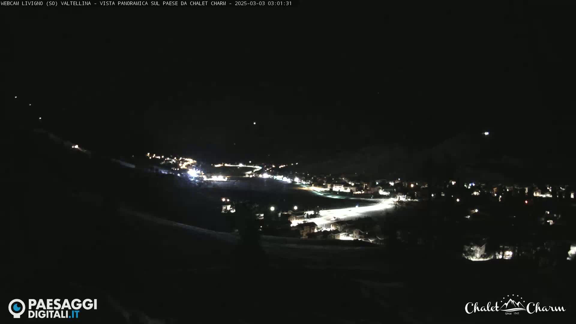 A nighttime, panoramic view of a snow-covered town illuminated by lights under a clear, dark sky.