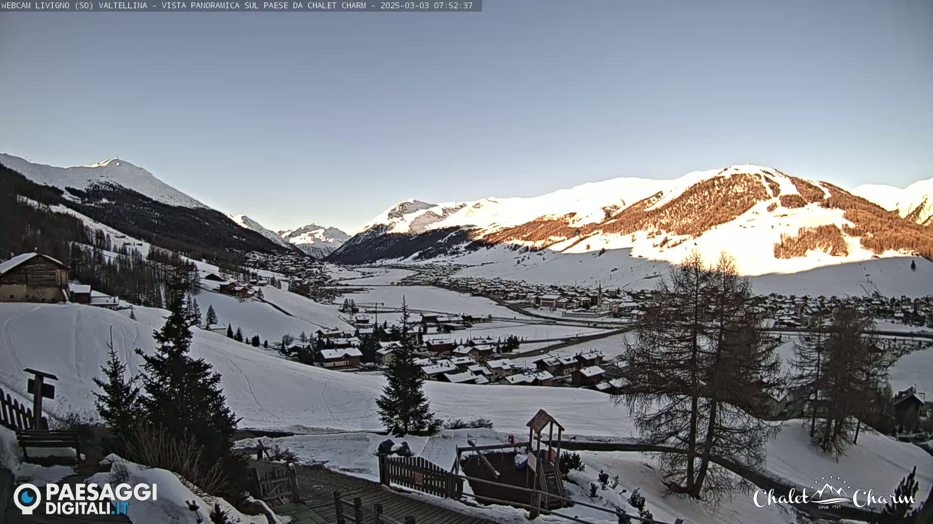 A snow-covered village nestled in a valley between snow-capped mountains under a clear, bright sky.