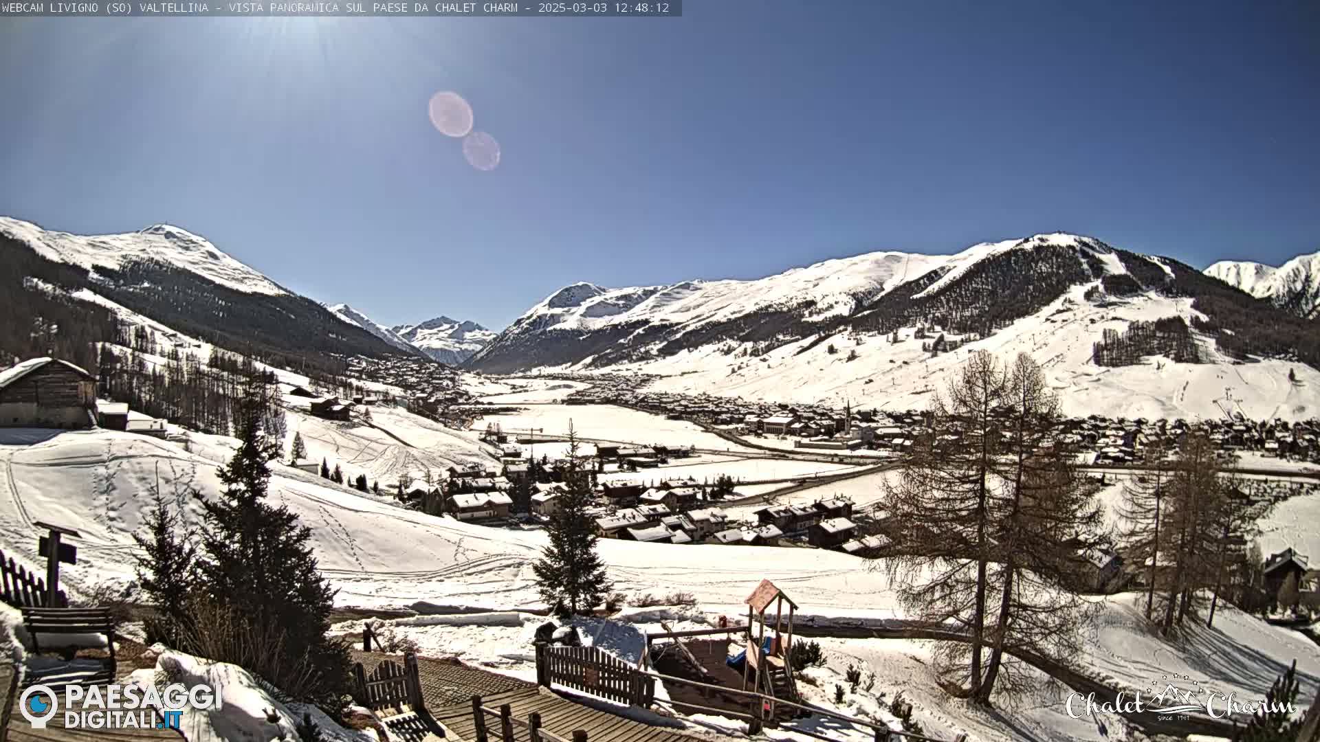 A snow-covered village nestled in a valley between snow-capped mountains under a clear, sunny sky.