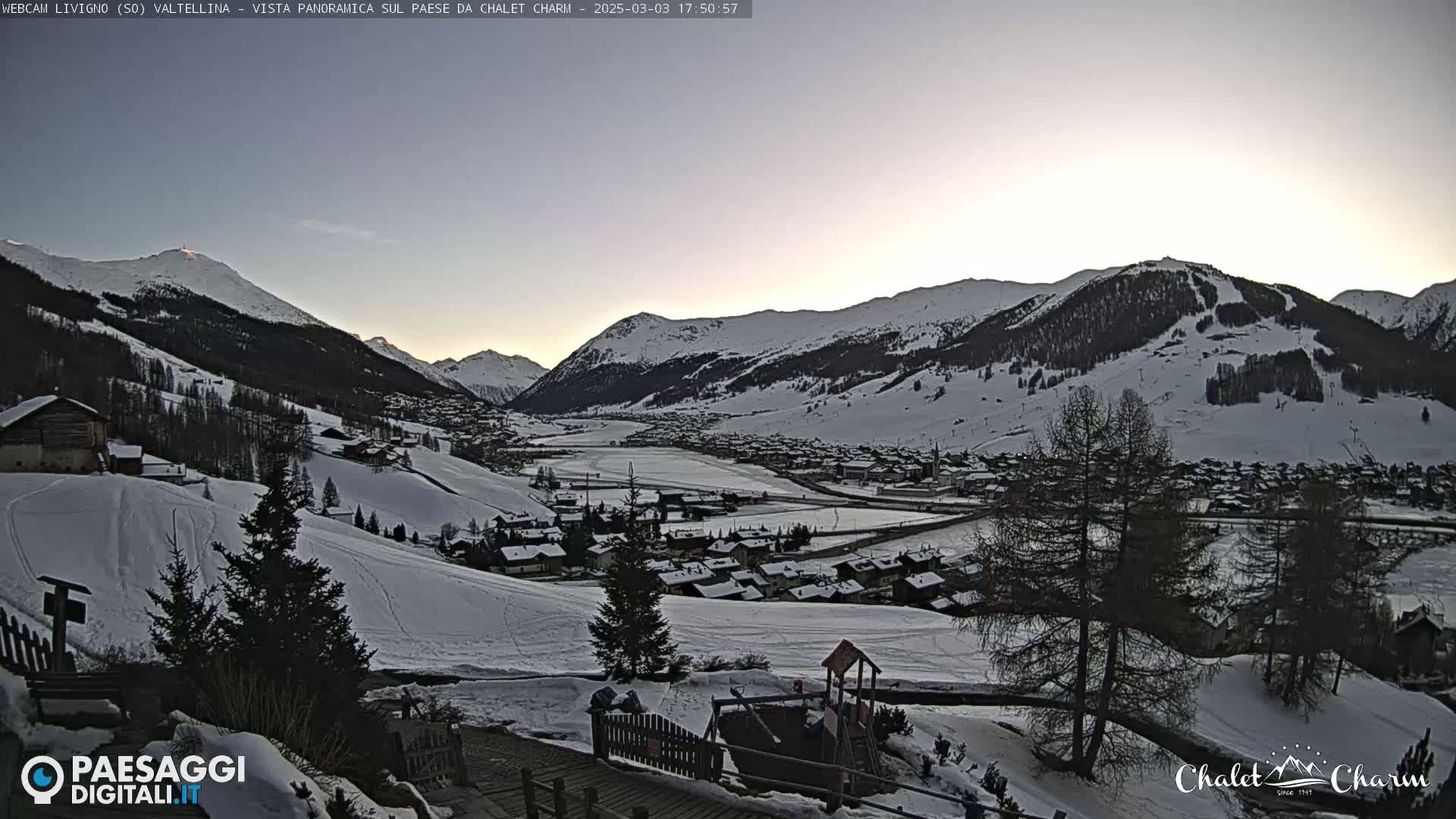 A snow-covered valley town nestled among snow-capped mountains at dusk.