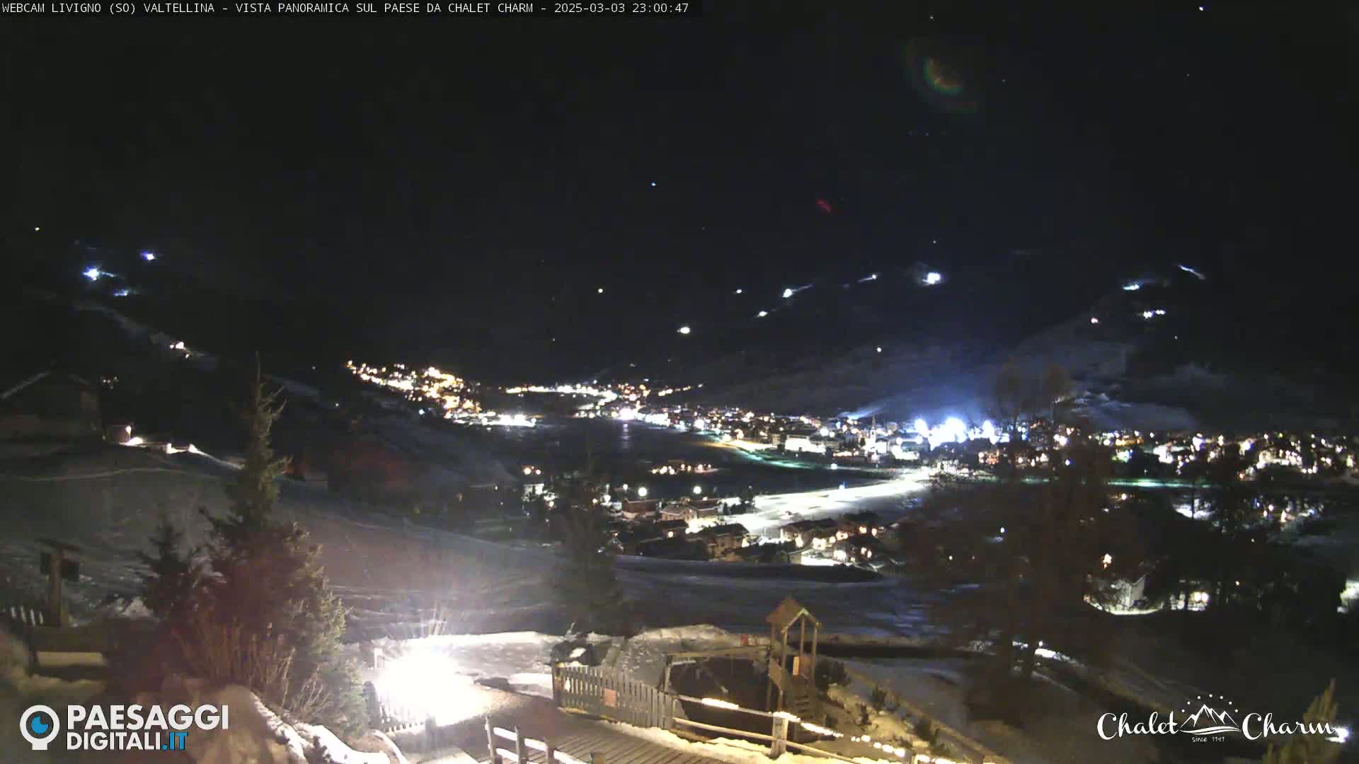 A nighttime, panoramic view of a snow-covered town illuminated by lights under a clear, starry sky.