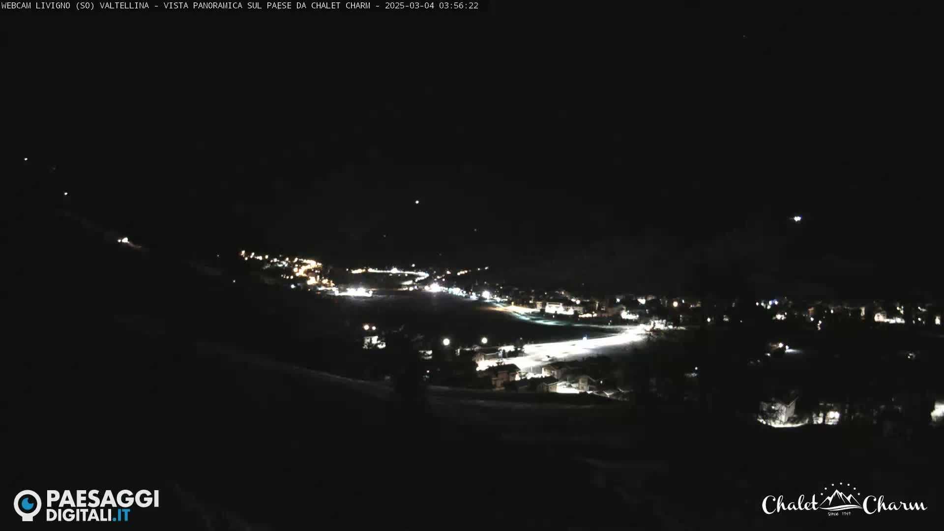 A nighttime, panoramic view of a snow-covered town illuminated by lights, under a clear, dark sky.