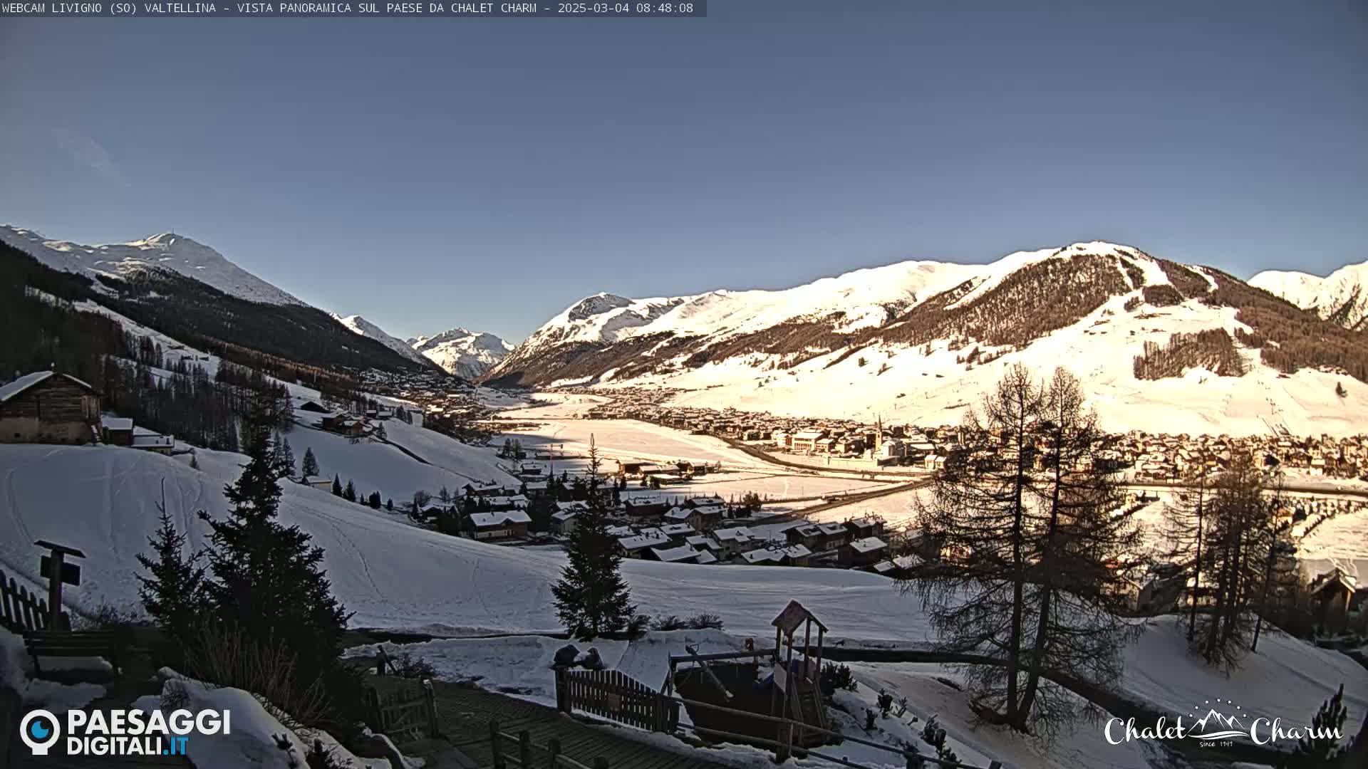 A snow-covered mountain village is seen from a hilltop on a sunny day.