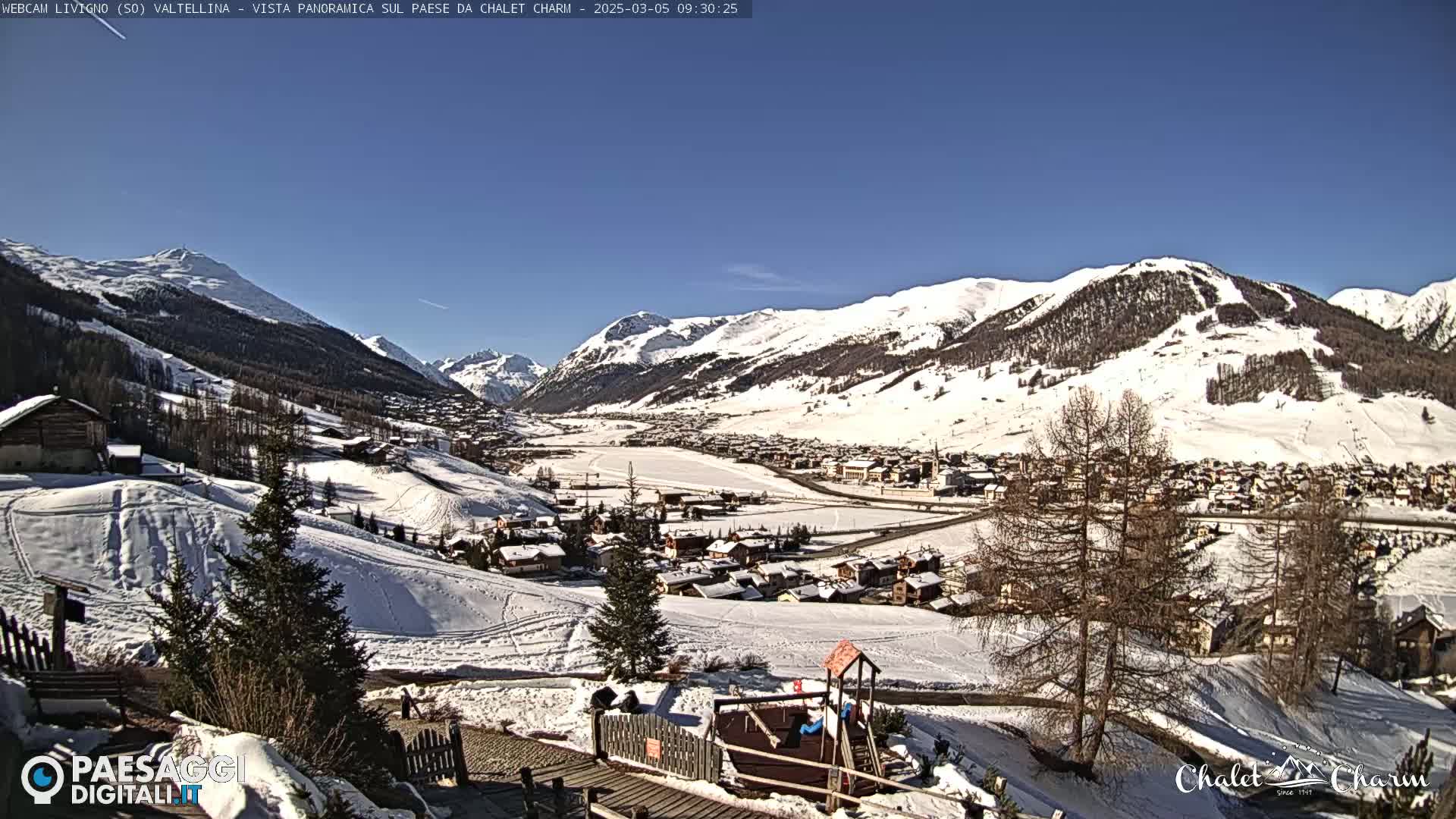 A snow-covered village nestled in a valley between snow-capped mountains under a clear blue sky.