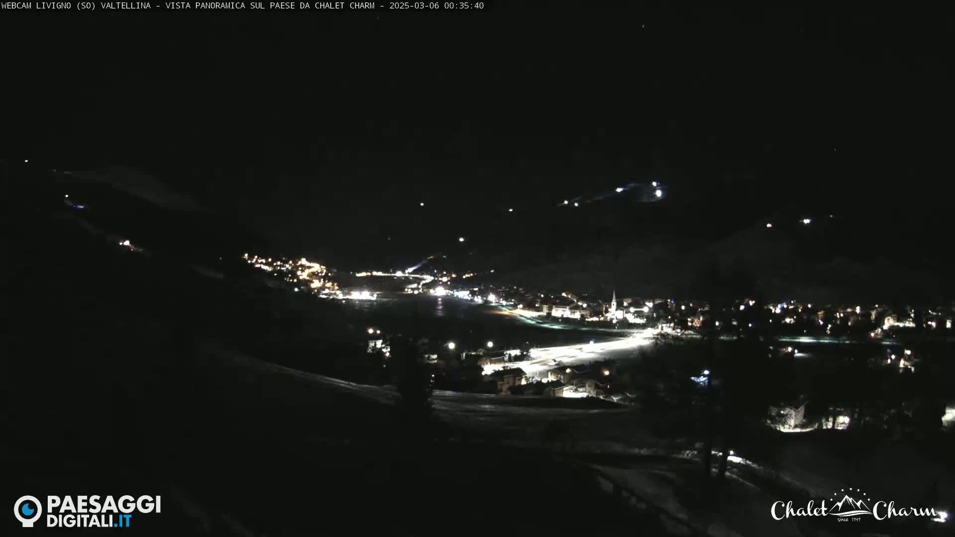 A nighttime, panoramic view of a snow-covered village illuminated by lights, under a clear, dark sky.