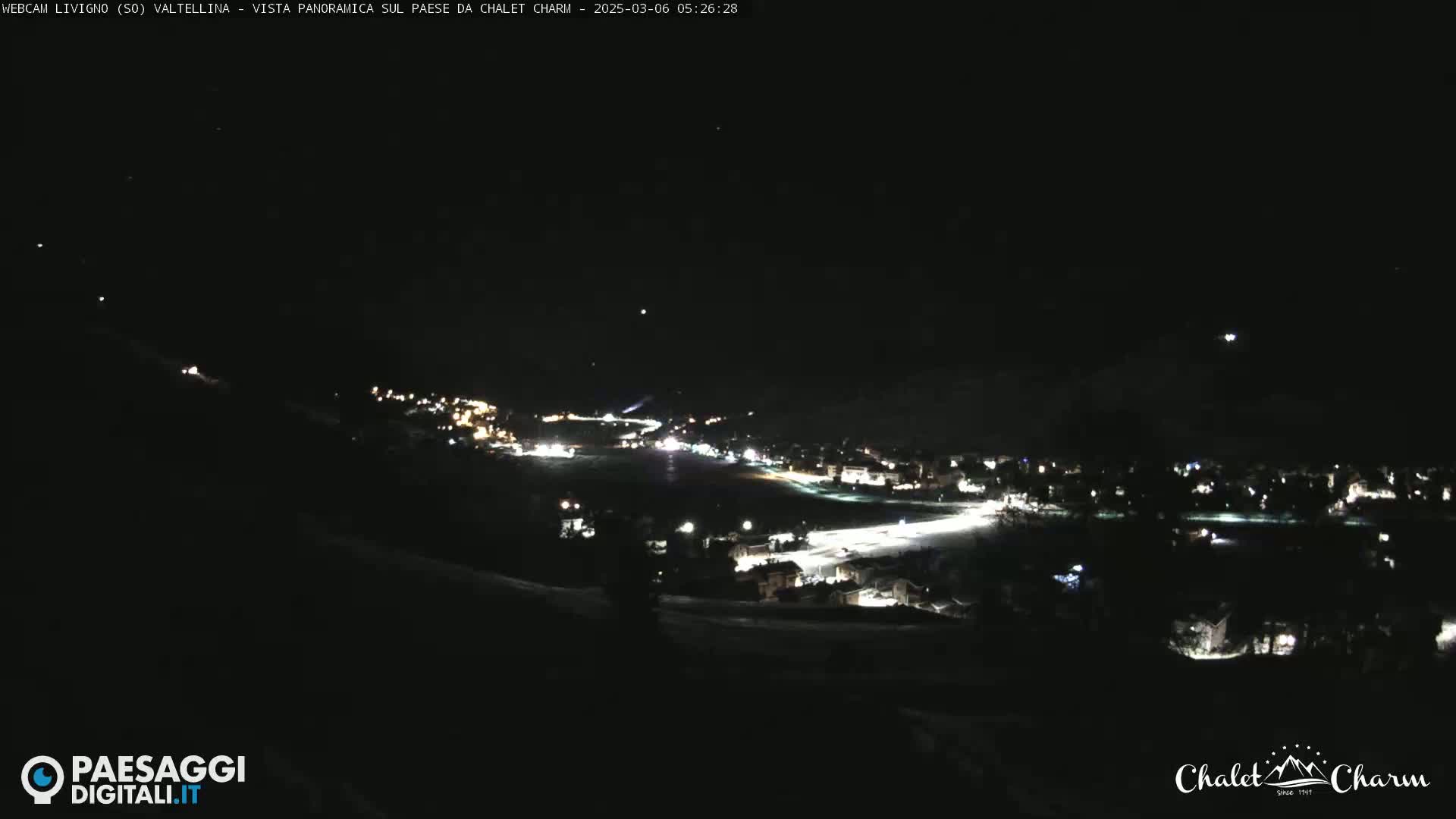 A nighttime panoramic view of a snow-covered town illuminated by streetlights under a clear, dark sky.