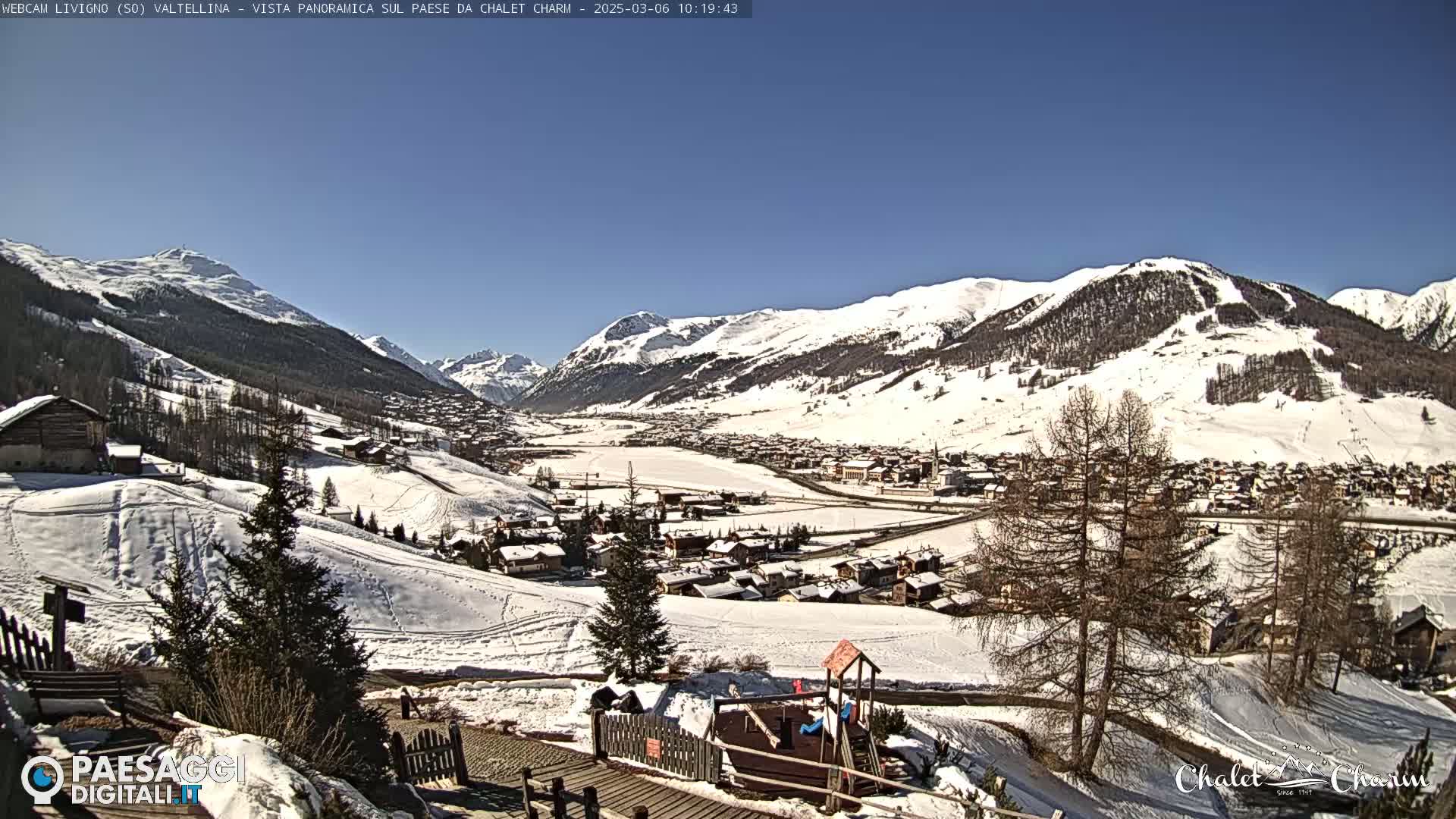 A snow-covered village nestled in a valley between snow-capped mountains under a clear blue sky.