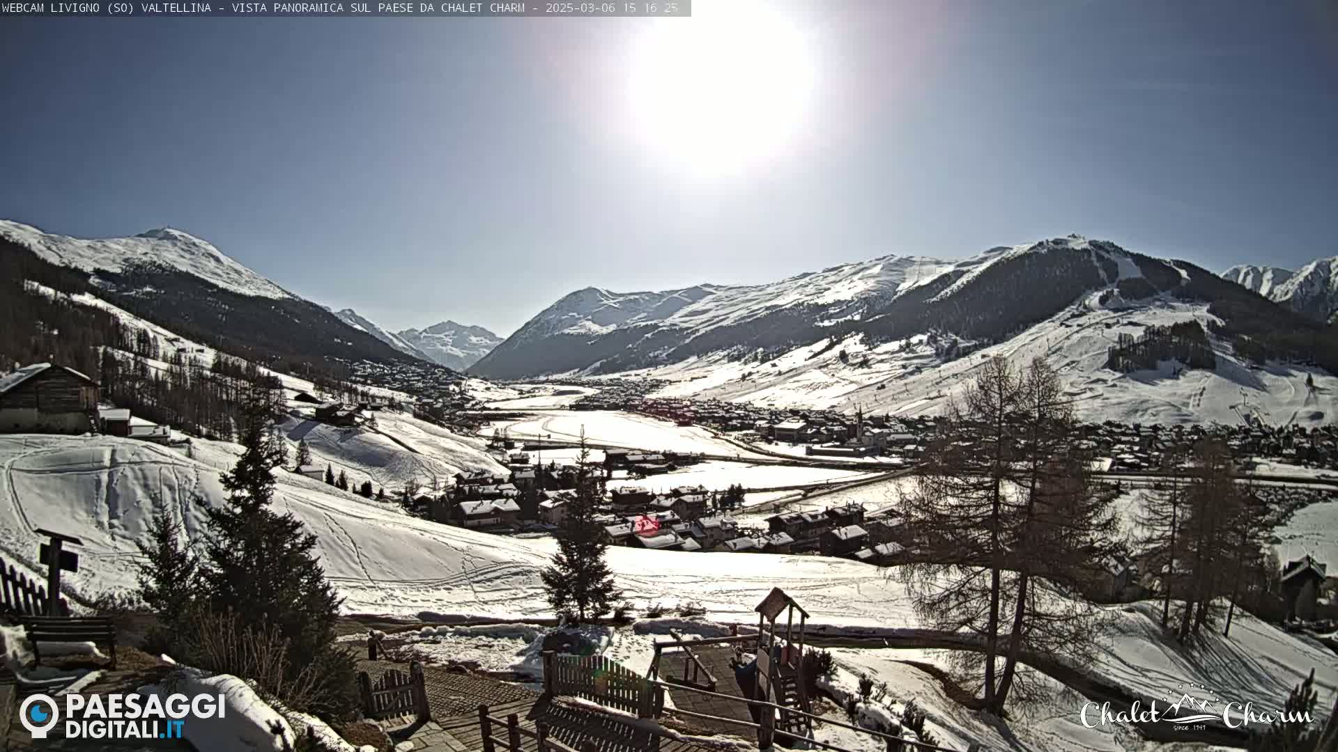 A sunny, snow-covered mountain valley town is viewed from a high vantage point, showcasing numerous buildings and ski slopes.
