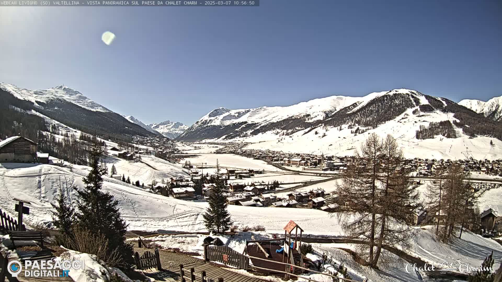 A snow-covered mountain village is viewed from a hillside on a sunny day.