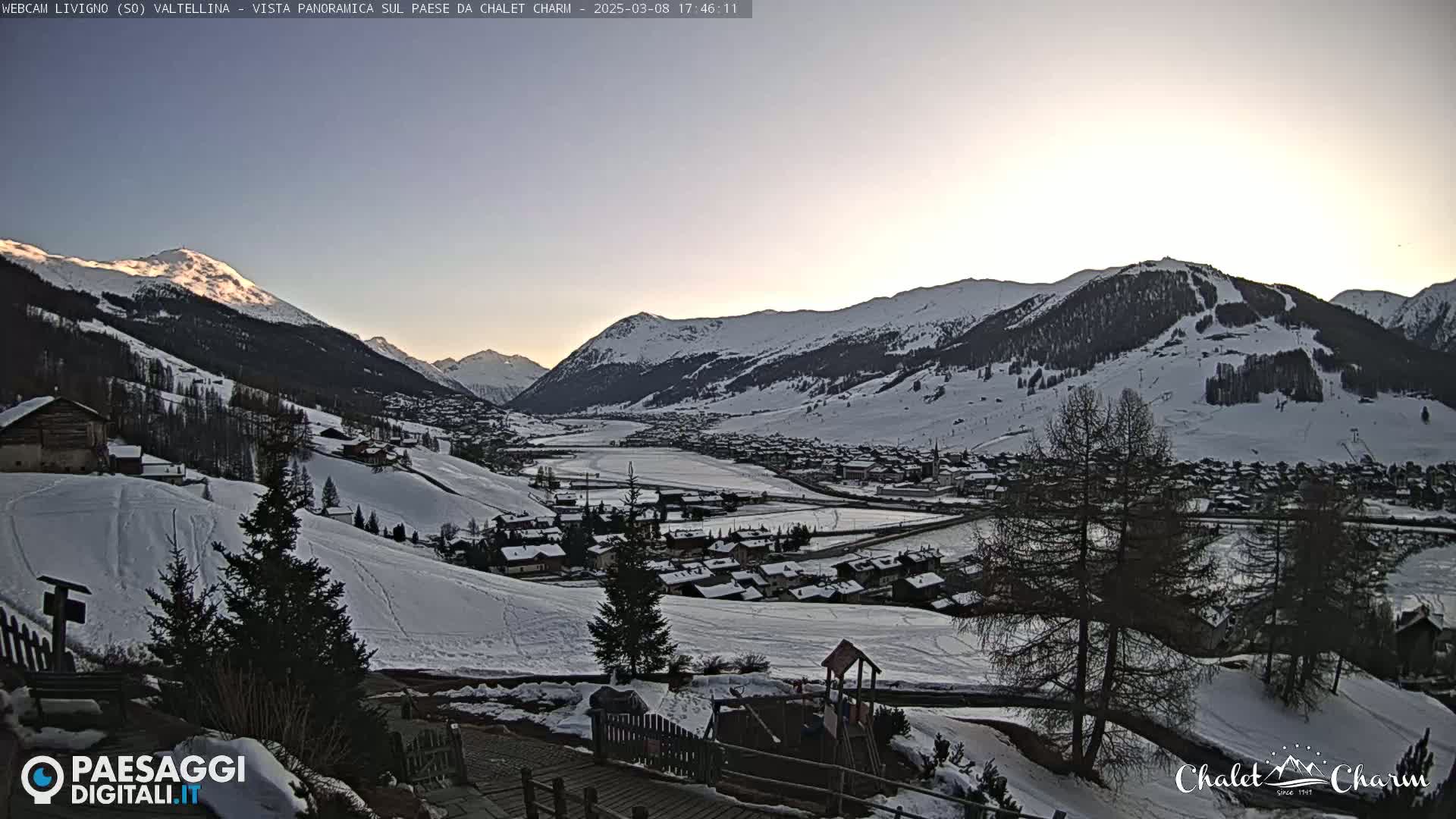 A snow-covered mountain village nestled in a valley at sunset, with snow-covered mountains in the background.