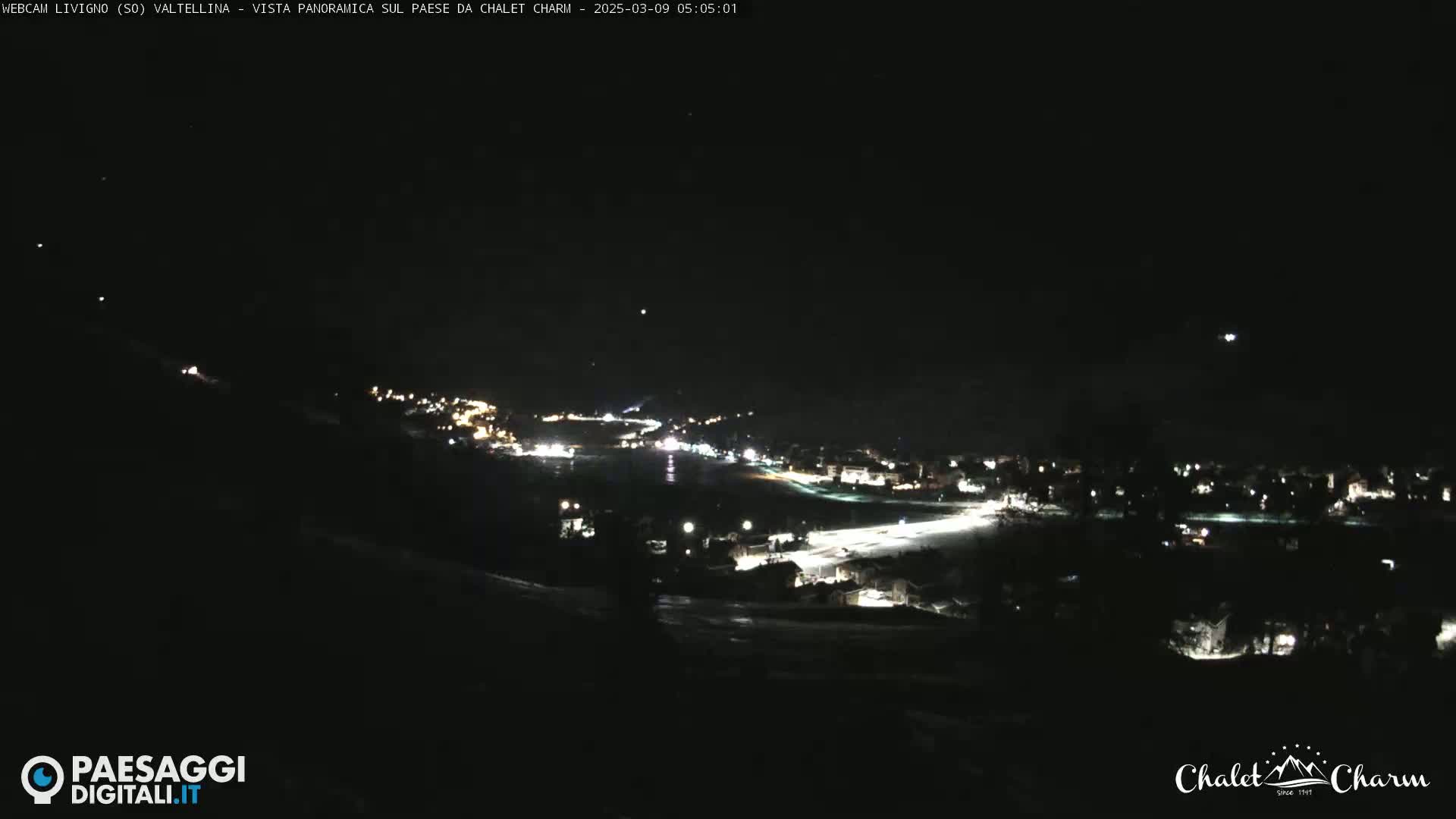 A nighttime panoramic view of a town illuminated by lights, under a clear, dark sky.
