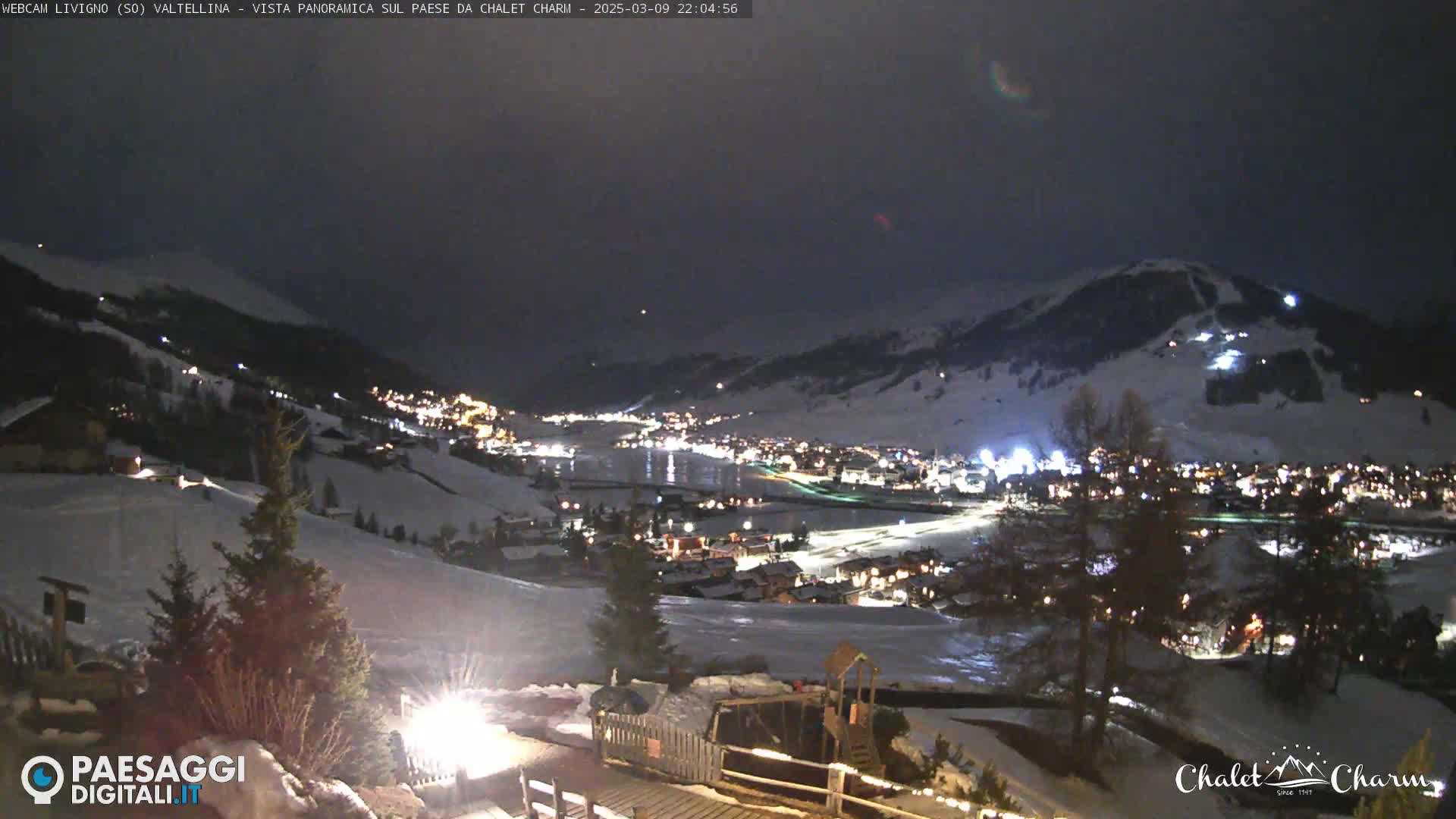 A nighttime panoramic view of a snow-covered town illuminated by lights, nestled in a valley beneath a dark, clear sky.