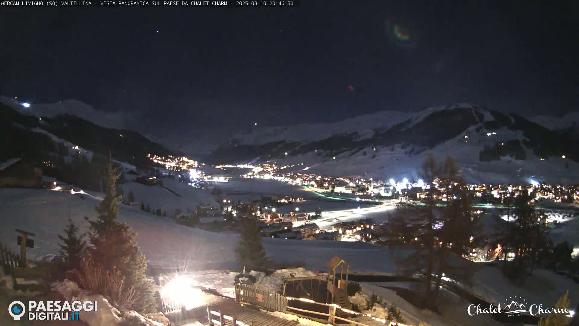 A nighttime, panoramic view of a snow-covered town nestled in a valley under a clear, dark sky.
