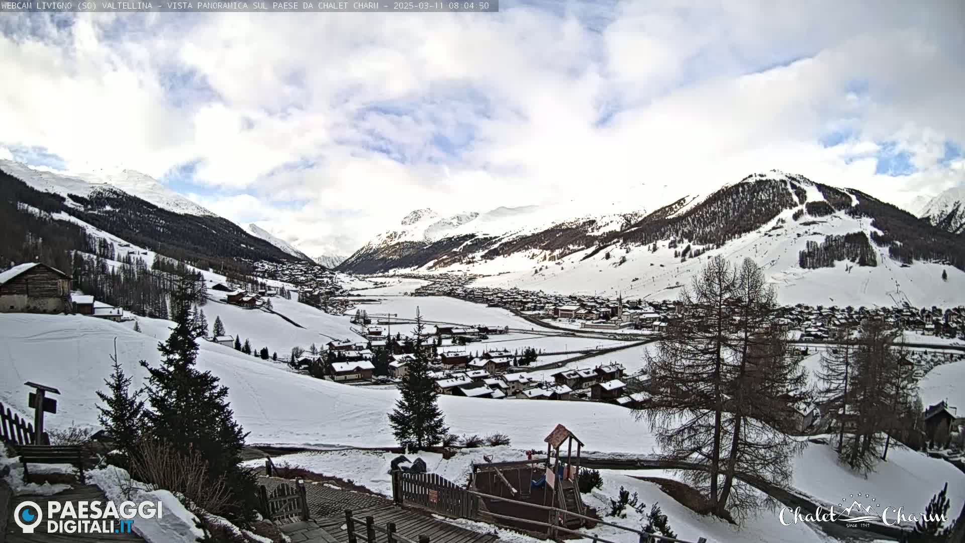 A snow-covered mountain village nestled in a valley under a partly cloudy sky.