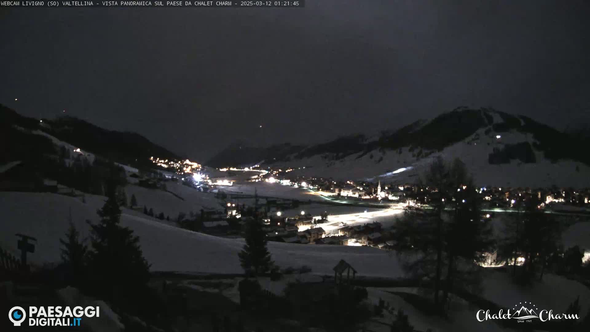 A snow-covered valley town is illuminated at night under a dark sky.
