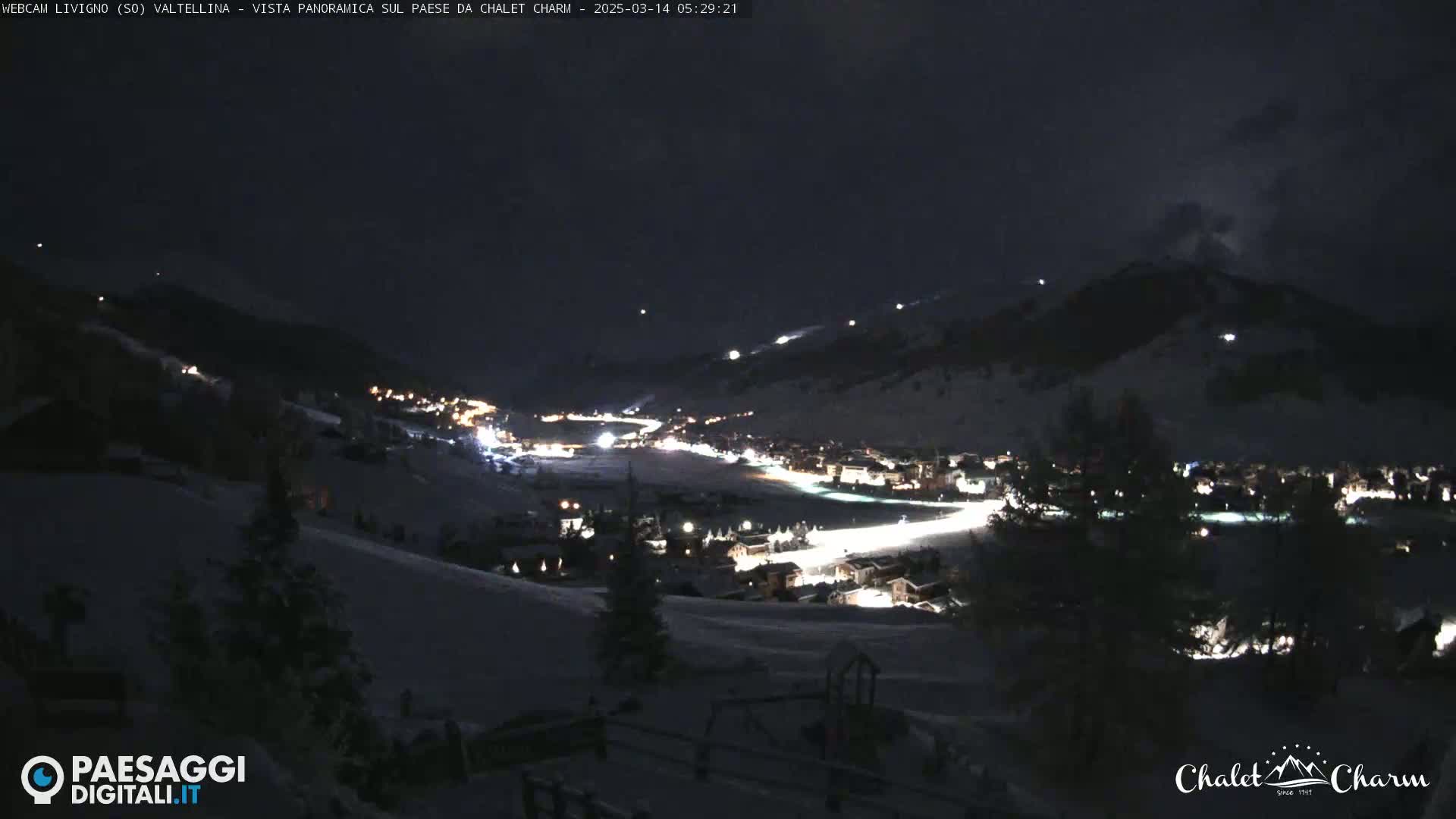 A snow-covered valley town is illuminated at night under a dark sky.