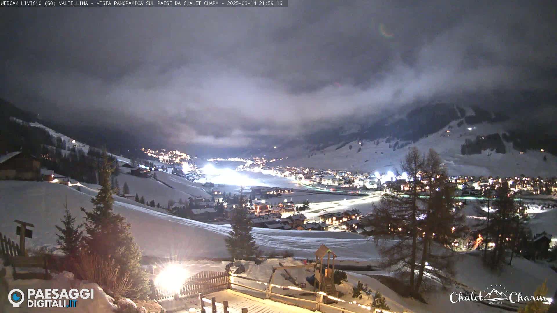 A snow-covered village at night is nestled in a valley under a cloudy sky.