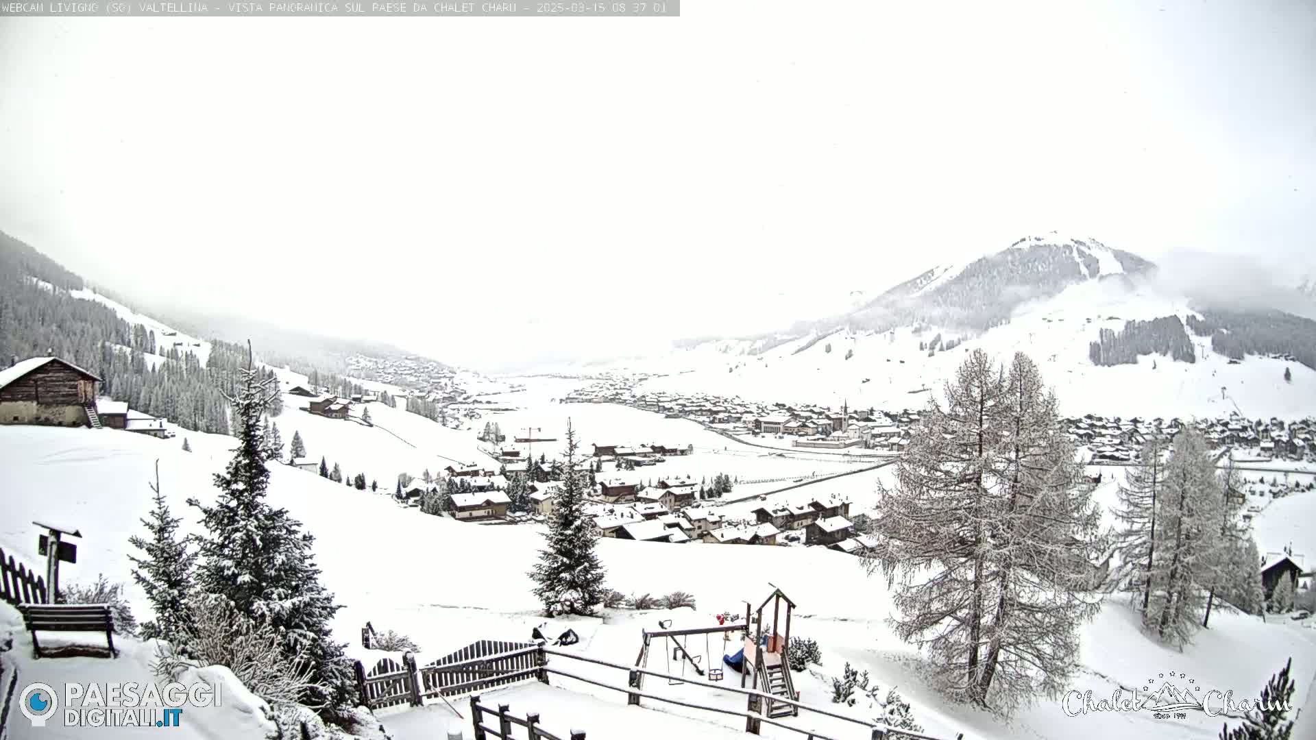 A snow-covered village nestled in a valley between snow-dusted mountains under an overcast sky.