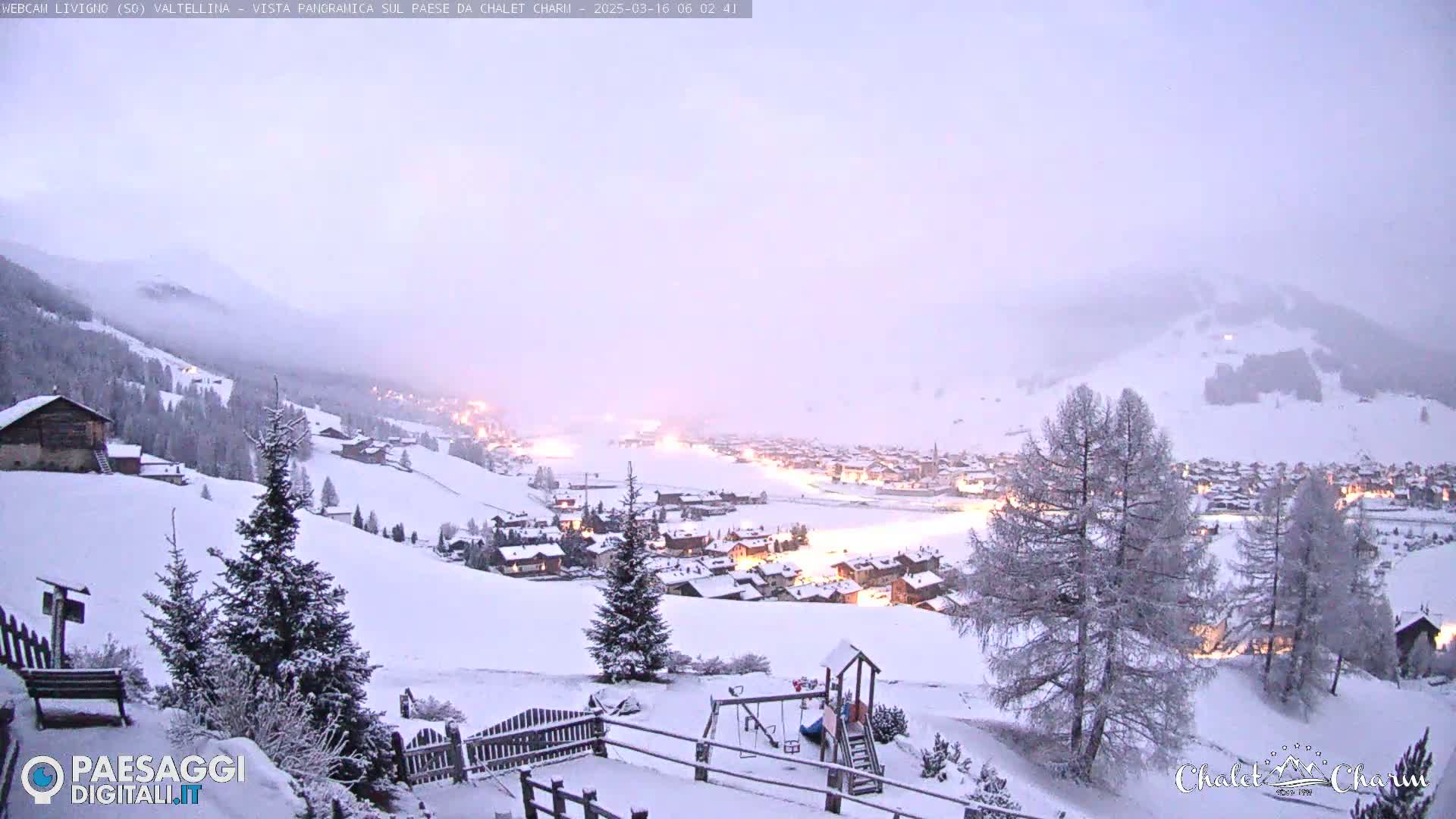A snow-covered village nestled in a valley is illuminated at twilight under a hazy sky.