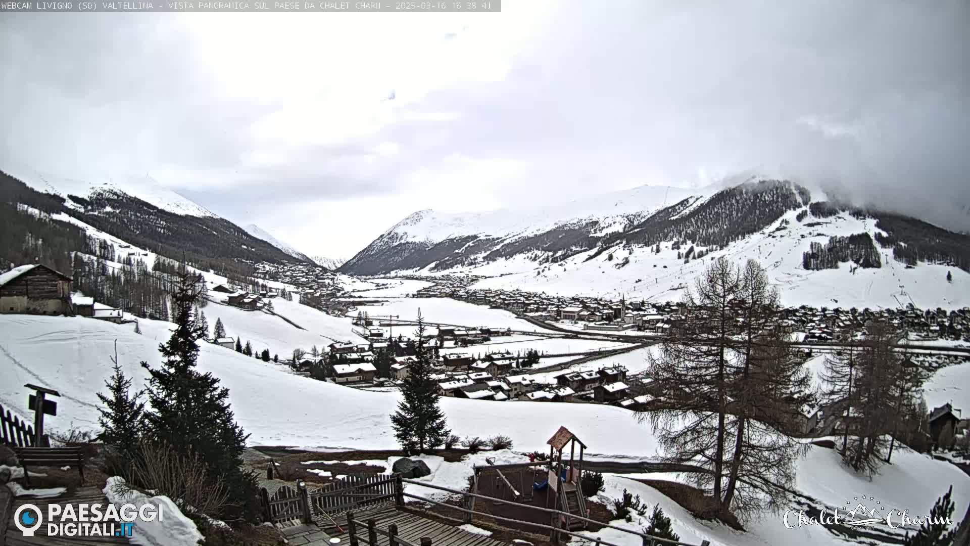 A snow-covered mountain village is viewed from a snowy hillside on an overcast day.