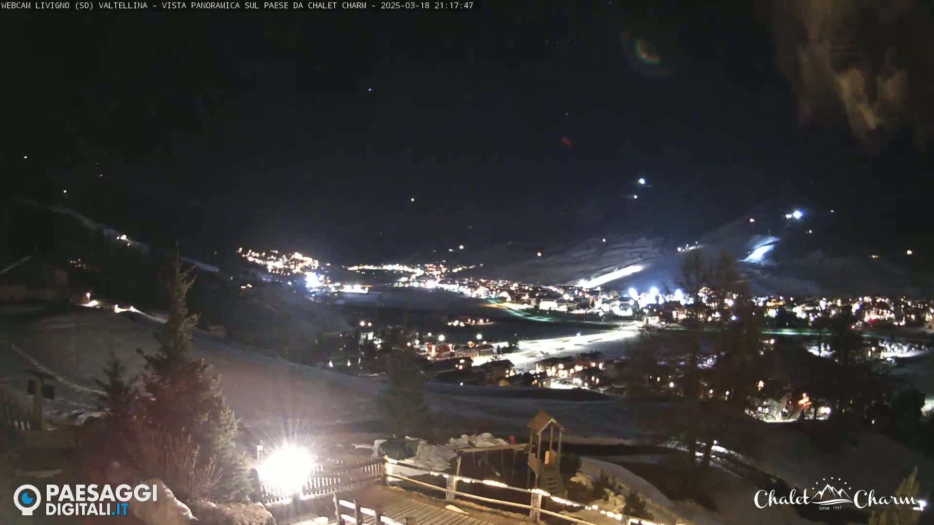 A nighttime, panoramic view of a snow-covered town illuminated by lights, under a clear, starry sky.