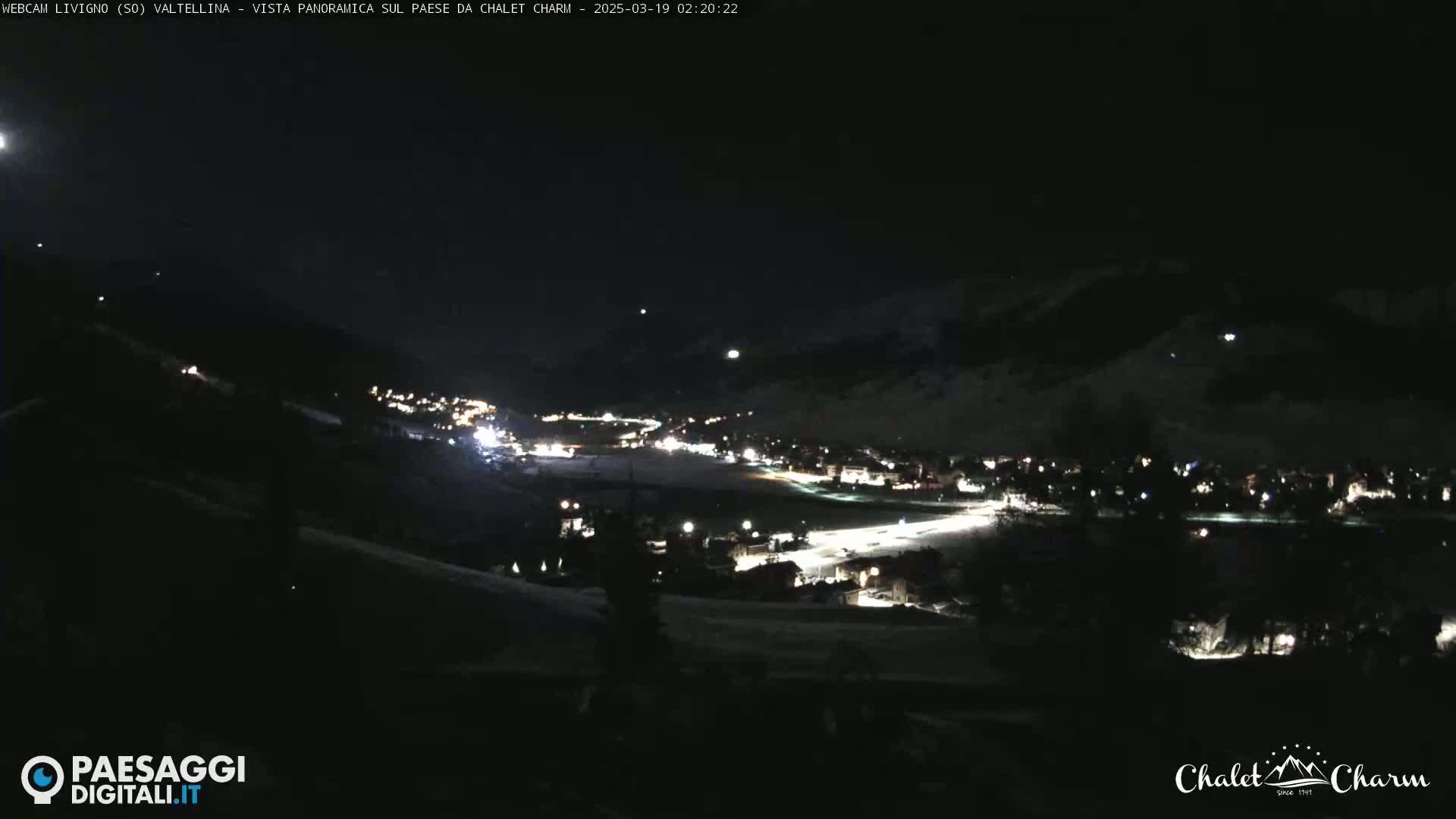 A nighttime, panoramic view of a snow-covered town illuminated by lights, under a dark, clear sky.