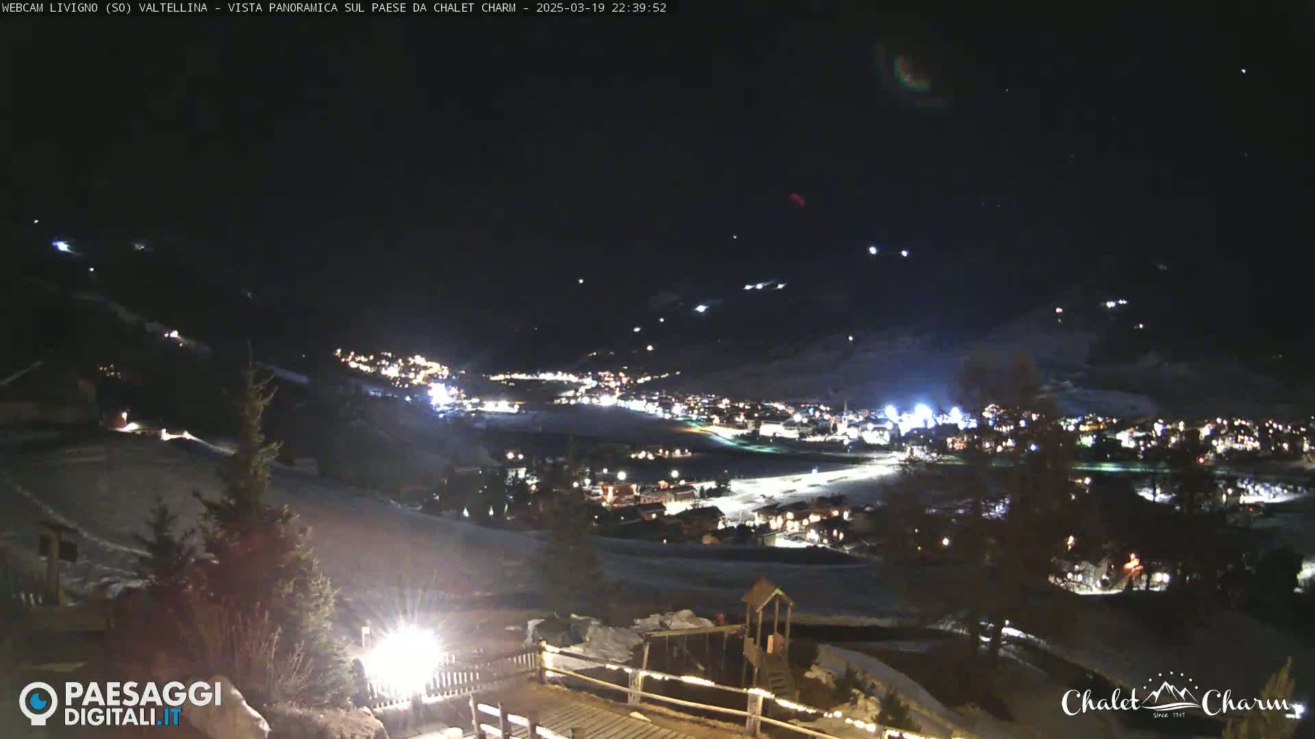 A nighttime panoramic view of a snow-covered village illuminated by lights, with a clear, dark sky above.