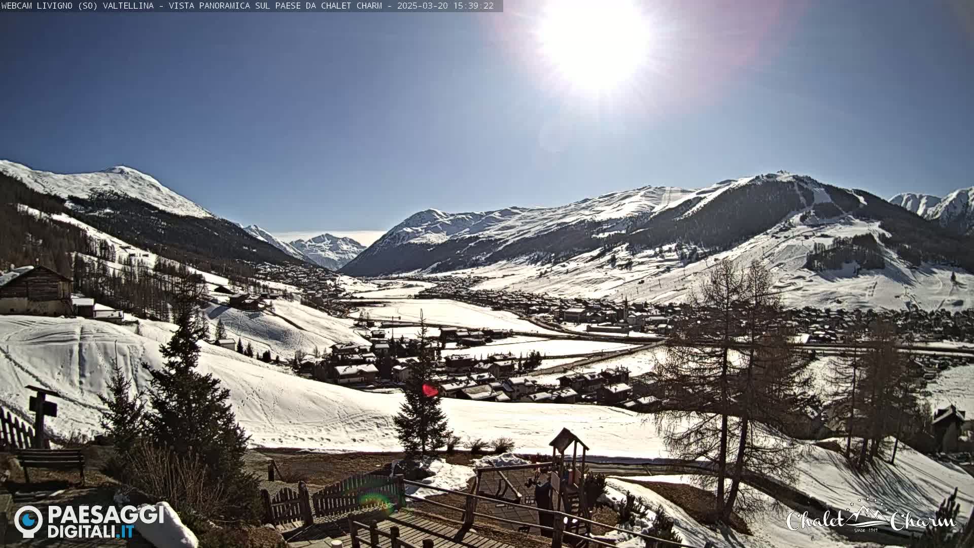 A sunny, snow-covered mountain valley town is viewed from a hillside, with a children's playground visible in the foreground.