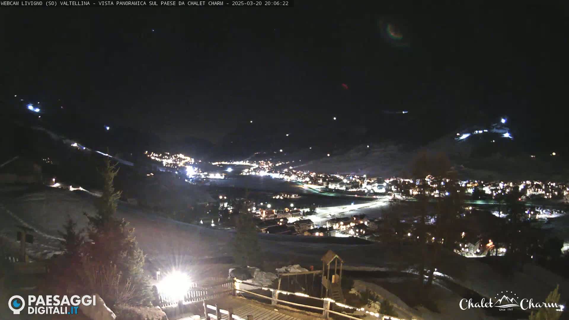 A nighttime panoramic view of a snow-covered town illuminated by lights, under a clear, dark sky.
