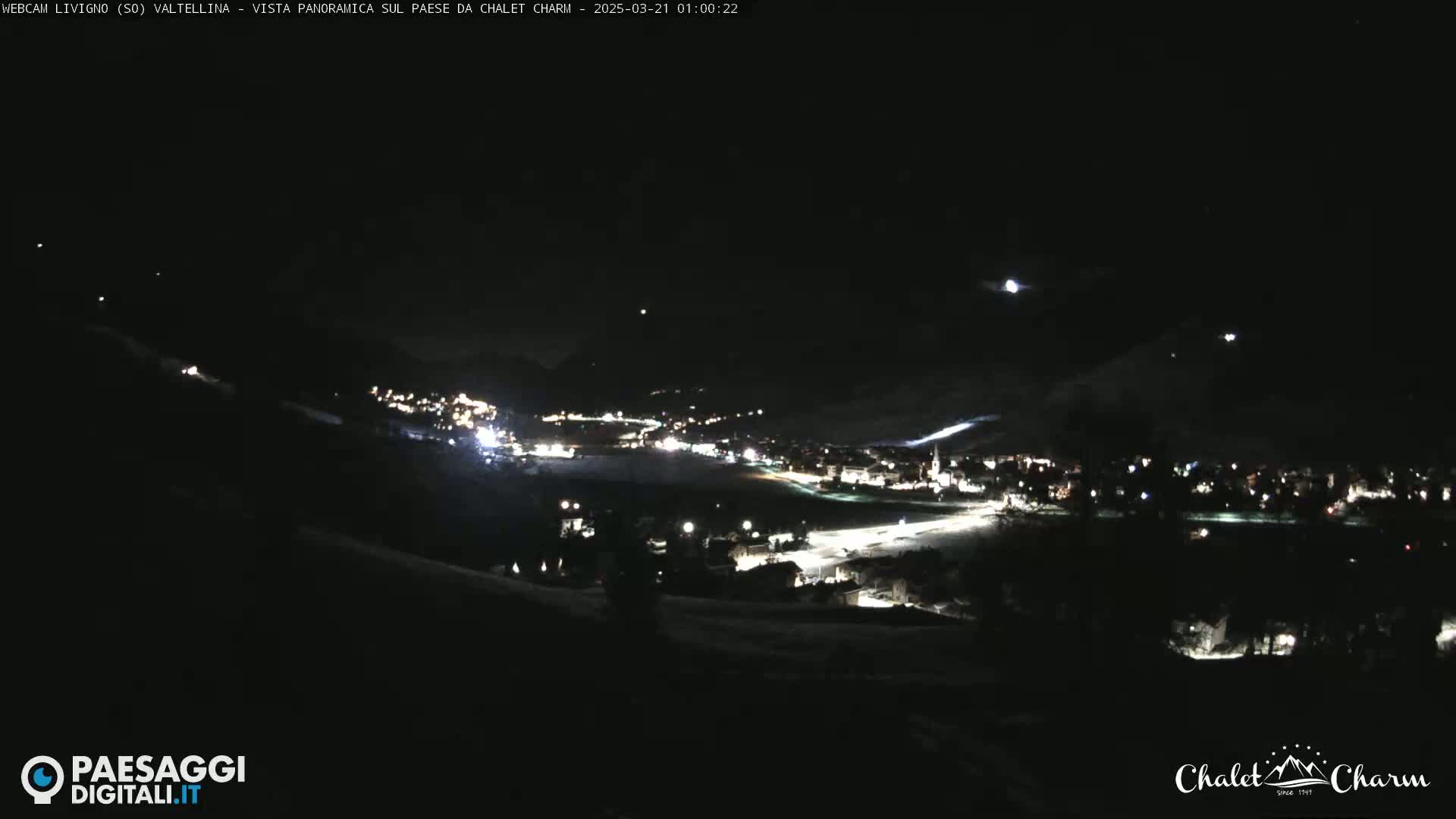 A nighttime panoramic view of a snow-covered town illuminated by lights, under a dark sky.