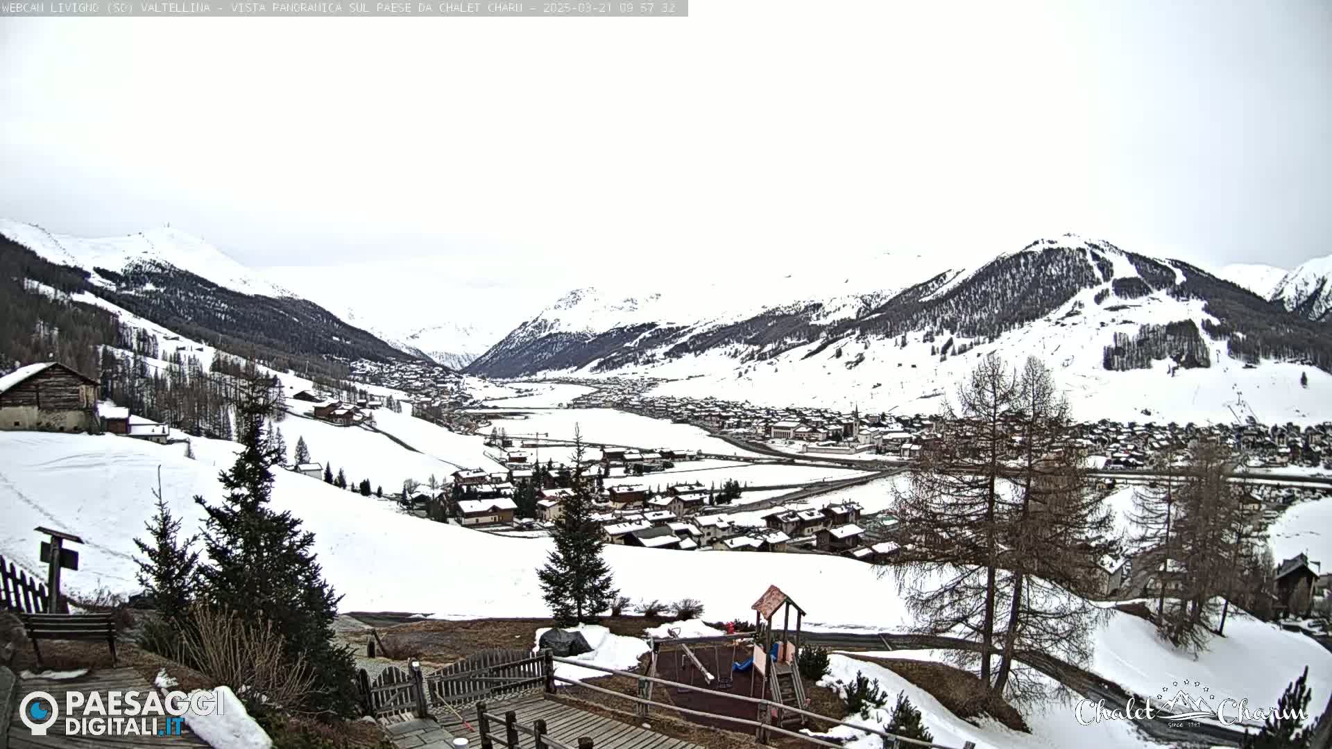 A snow-covered mountain valley town is viewed from a slightly elevated position, with overcast skies.