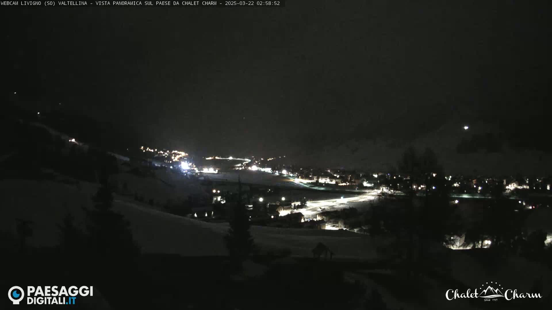 A nighttime, snow-covered landscape shows a small town illuminated with scattered lights under a dark sky.