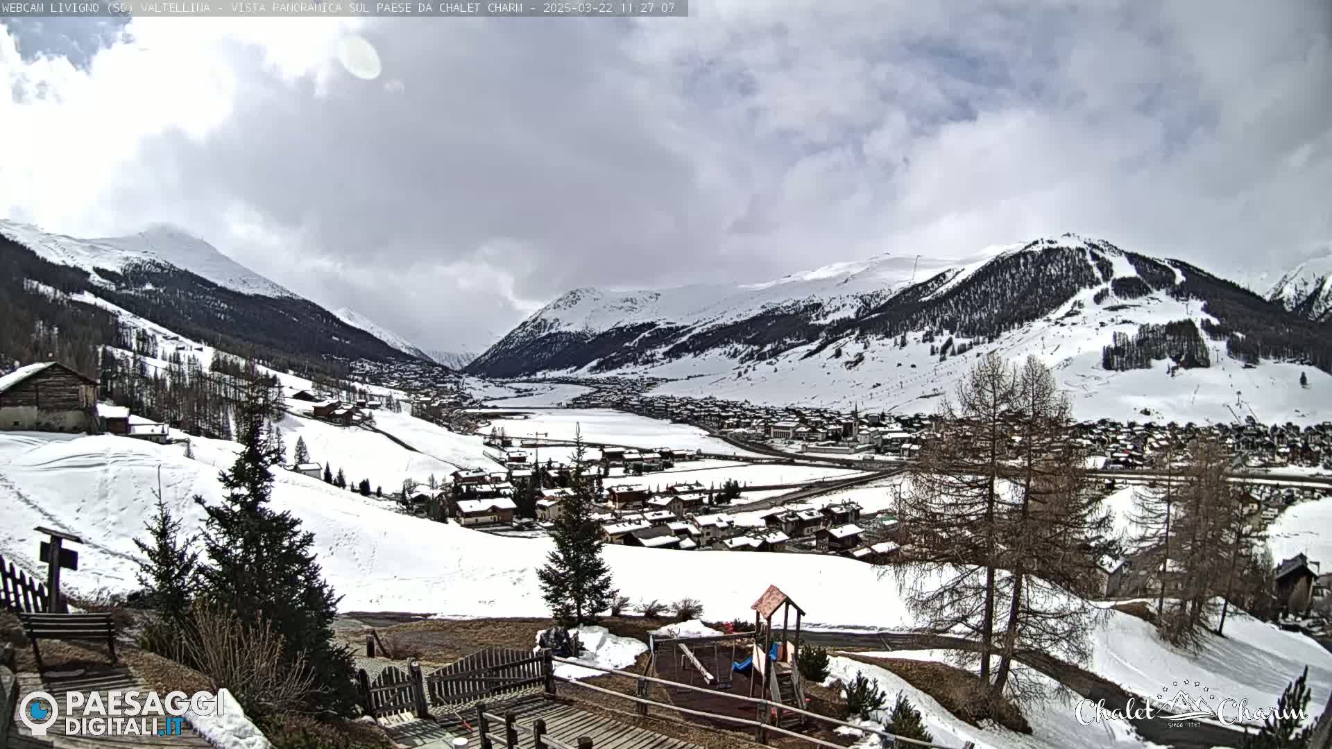 A snow-covered mountain village nestled in a valley under a partly cloudy sky.