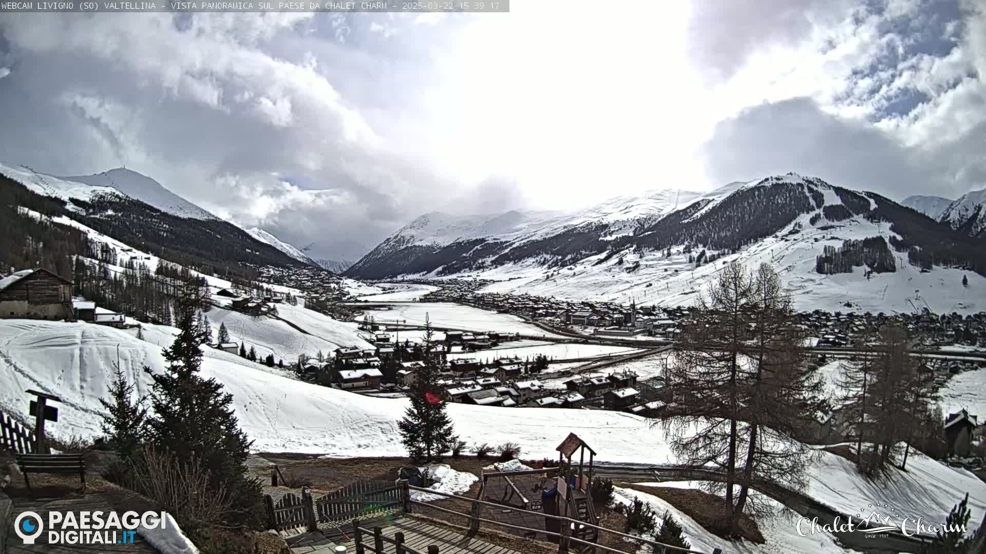 A snow-covered mountain village is visible from a high vantage point under a partly cloudy sky.