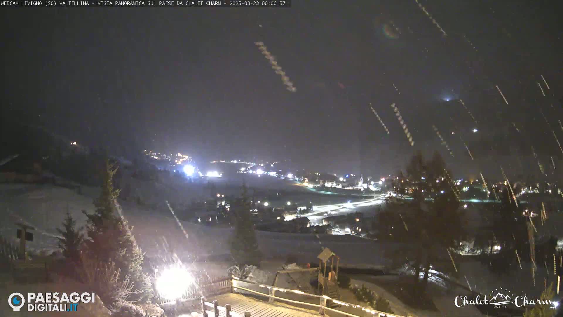 A nighttime panoramic view of a snow-covered town, illuminated by lights, with heavy snowfall.