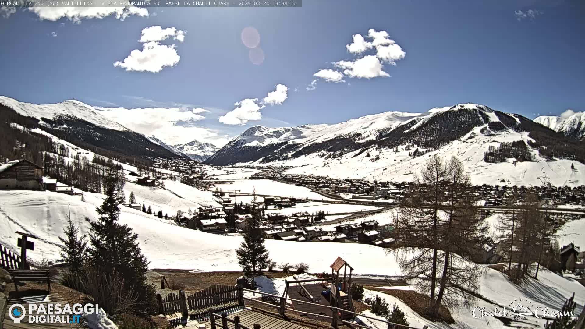 A snow-covered mountain valley town is seen on a partly sunny day, with a playground visible in the foreground.