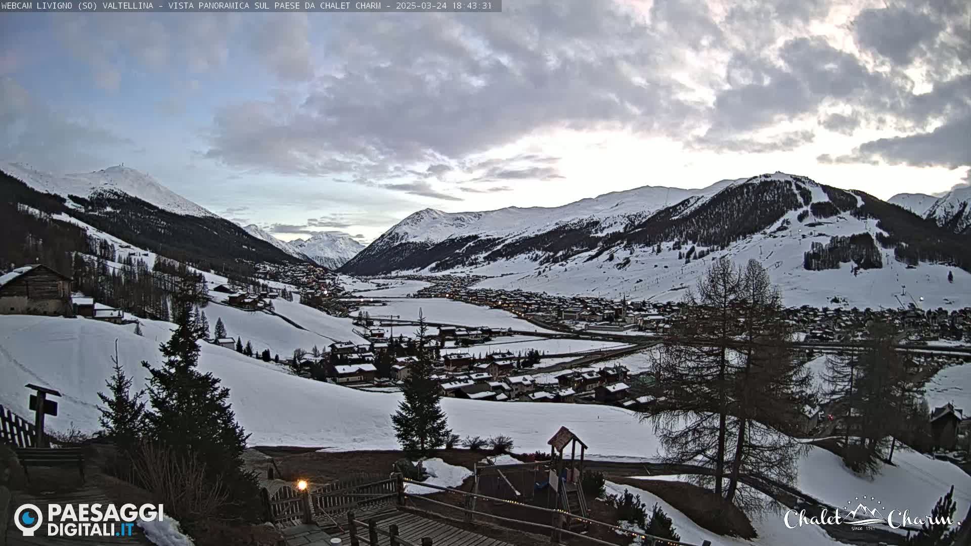 A snow-covered mountain village is nestled in a valley under a cloudy sky.