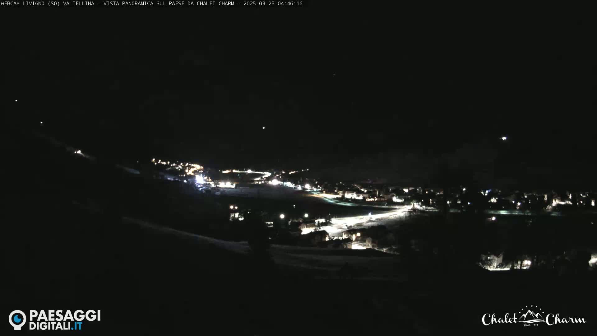 A nighttime panoramic view of a snow-covered town illuminated by scattered lights.