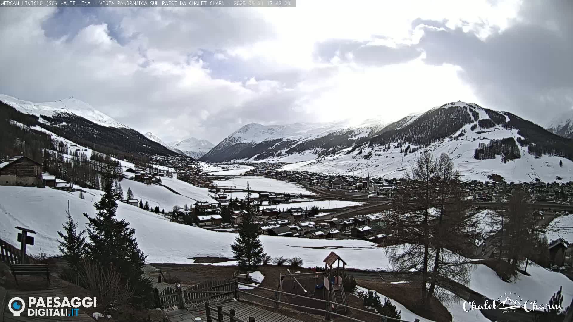 A snow-covered mountain valley town is seen under a partly cloudy sky.