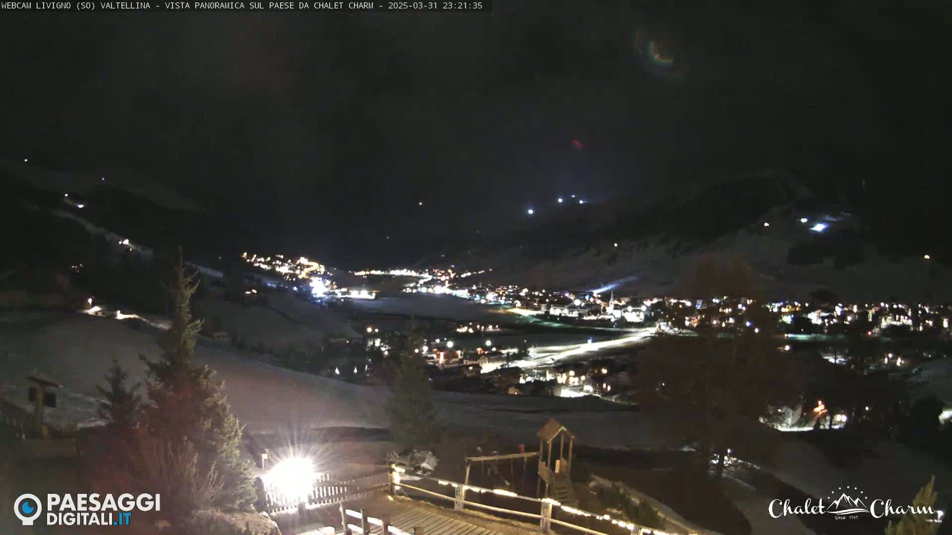 A nighttime, panoramic view of a snow-covered town illuminated by lights, nestled in a valley under a dark, clear sky.