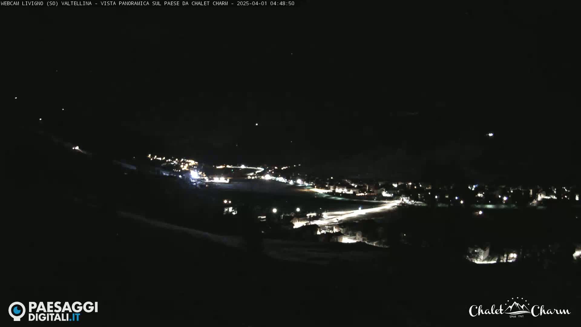 A nighttime long shot of a town illuminated by streetlights, nestled in a dark, snowy landscape under a clear, starlit sky.