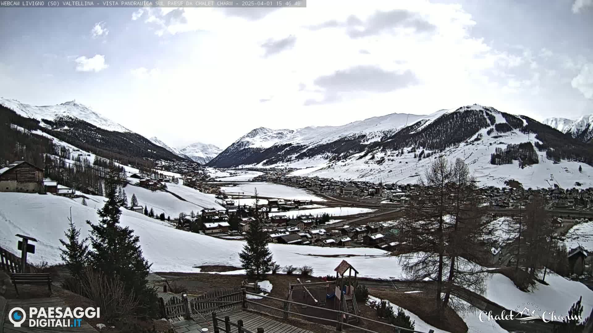 A snow-covered mountain village nestled in a valley under a partly cloudy sky.