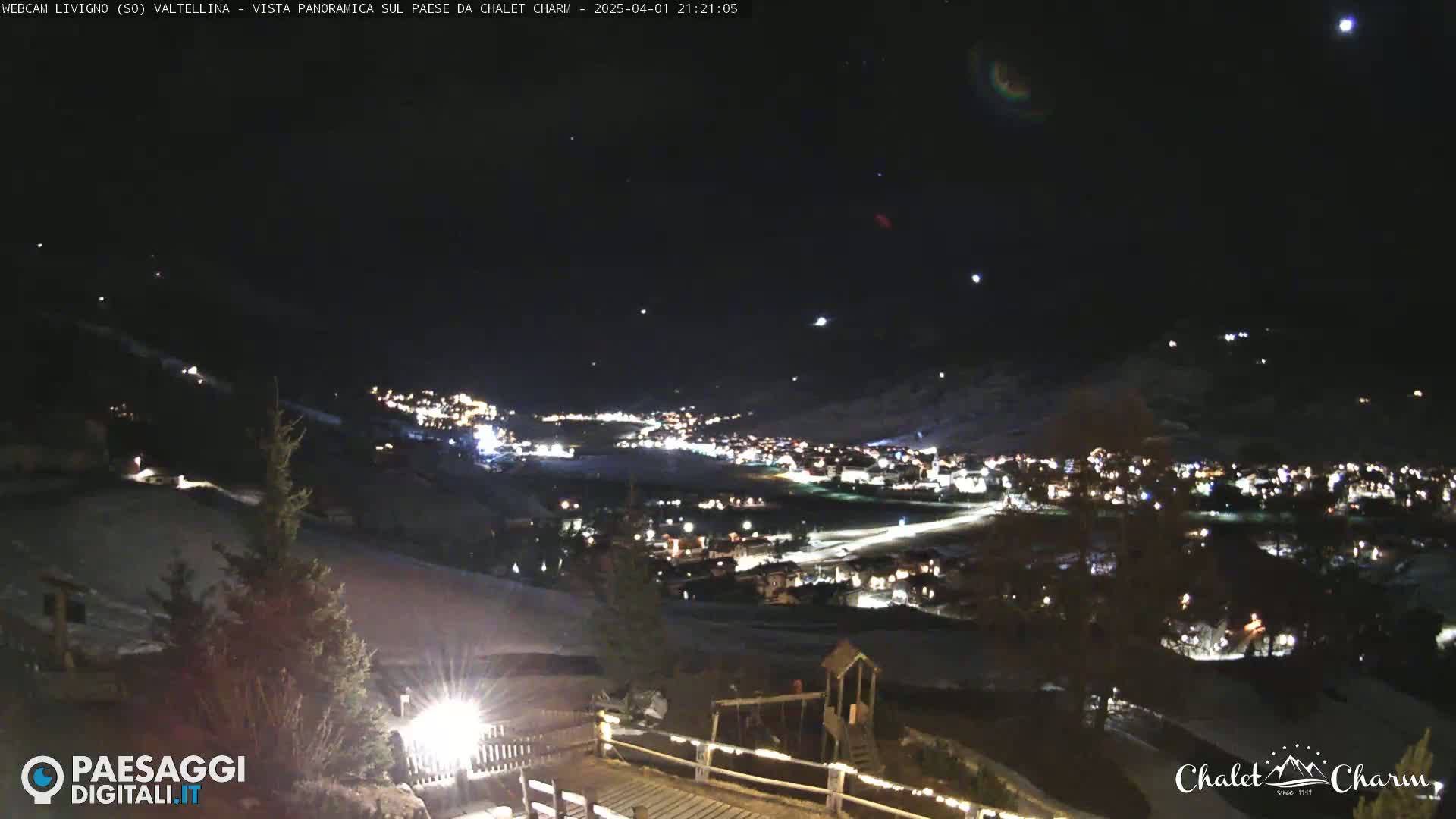 A nighttime panoramic view of a snow-covered village illuminated by lights under a clear, starry sky.
